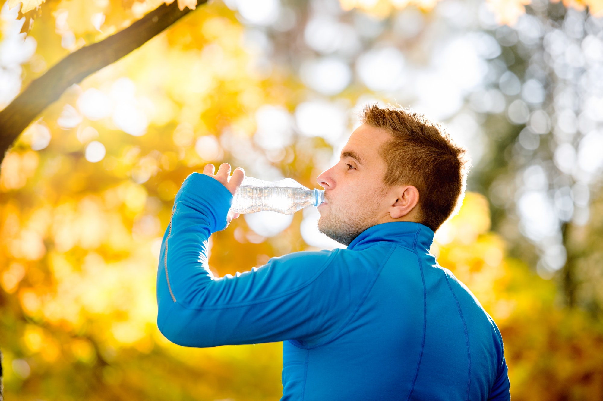 Hipster runner in autumn nature drinking water from bottle