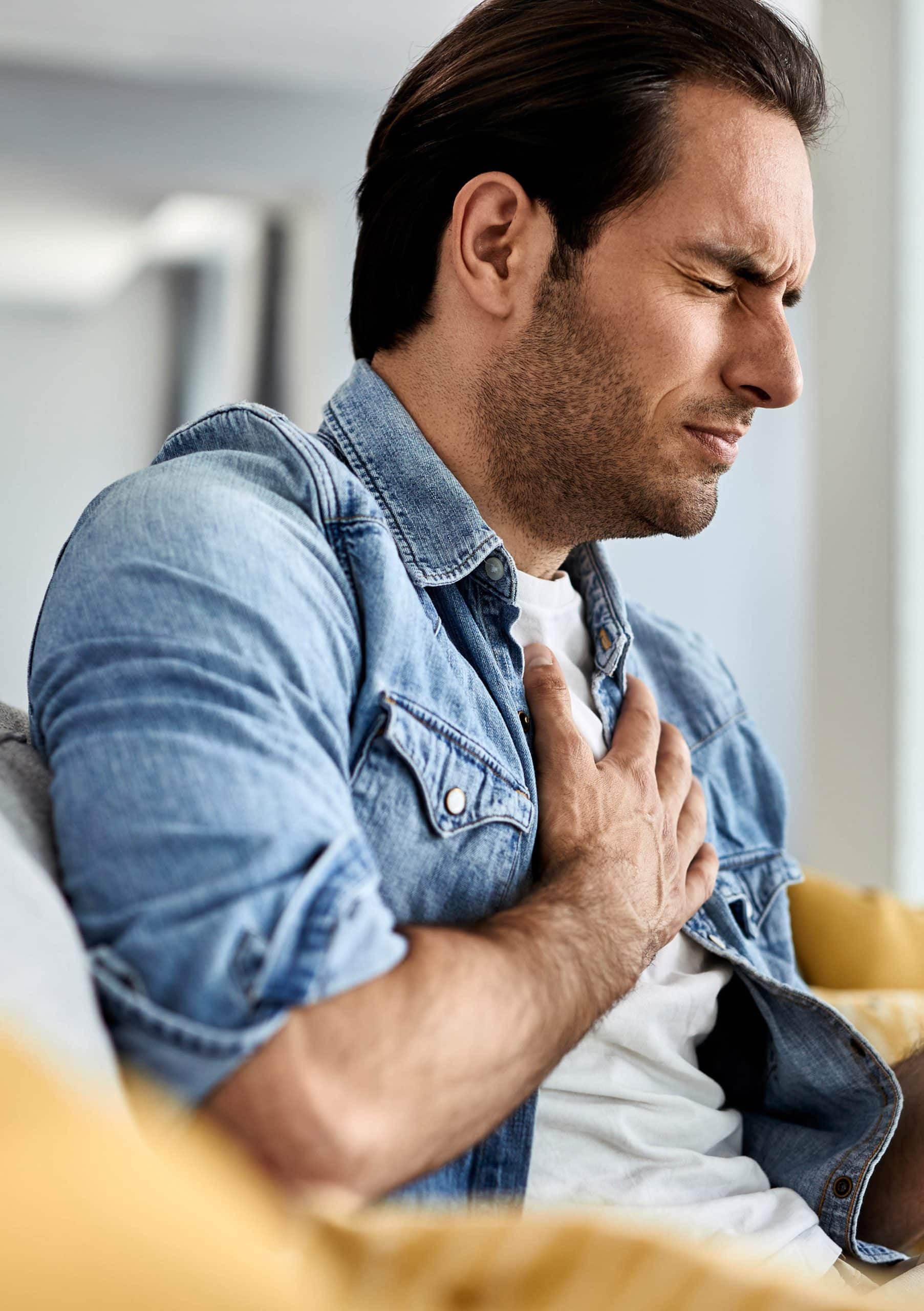 young-man-feeling-sick-holding-his-chest-pain-while-drinking-tea-living-room-scaled